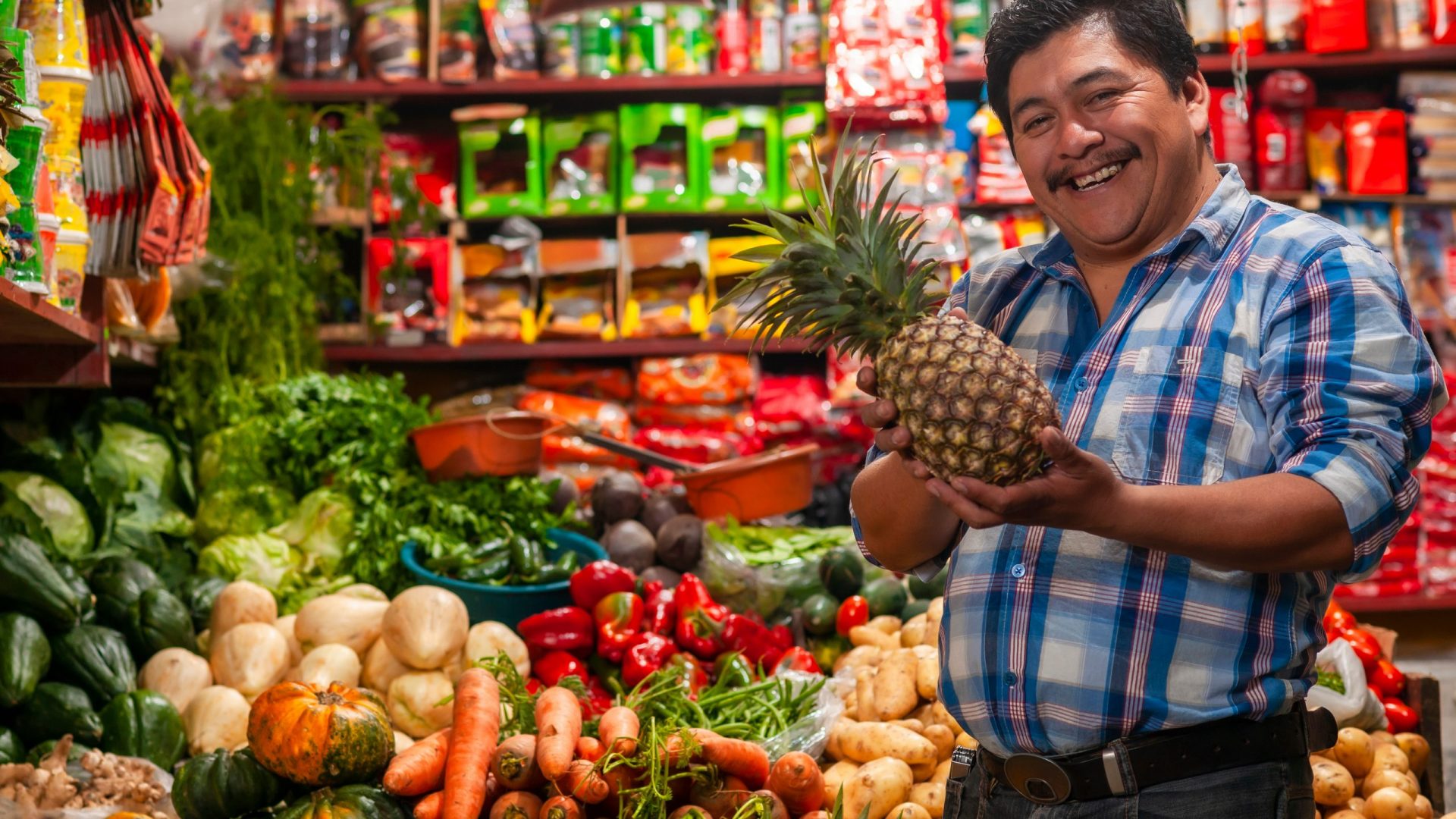 Seller holding a pineapple, in his grocery store.